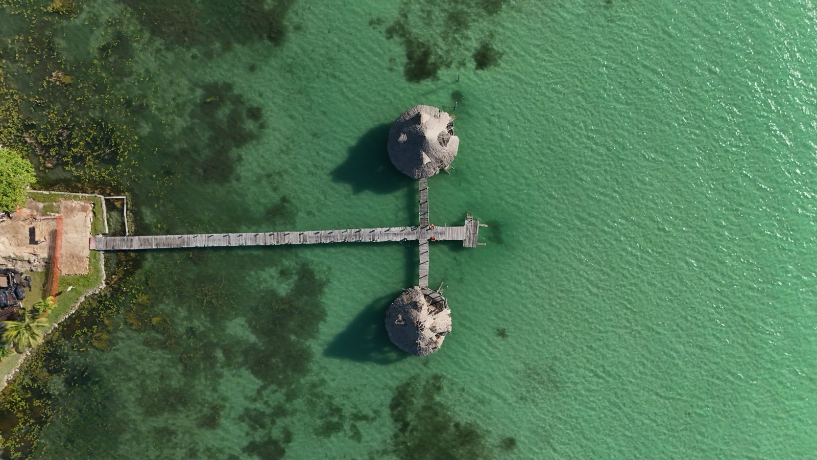 Aerial view of a wooden pier and palapas over the turquoise water of the Bacalar lagoon